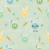 a repeating pattern of smiling rabbit faces and carrots against a light green background with stars. The pattern is described as a "smitten cotton" and "2.5 cm" in the provided text.
