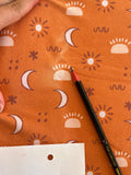 a hand holding a pencil over a patterned fabric with various sun and moon designs.
