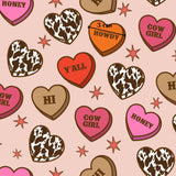 a pattern of heart-shaped candies with various sayings and designs, such as "Honey", "Howdy", "Yall", "Hi", "COW GIRL", and "Honey". The candies are scattered across a pink background with stars, creating a playful and whimsical visual effect.
