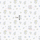 The image is a repeating pattern of blue flowers and green leaves on a white background, with a measurement scale in the center indicating the size of the pattern.