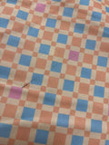a close-up view of a fabric with a checkered pattern of blue and orange squares. There is a small black mark or stain on the fabric, which is the only visible detail in the image.