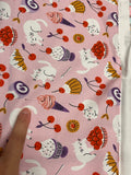 a close-up view of a fabric with a repeating pattern of cats and various desserts, such as cherries and cakes, printed on it.