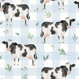 a repeating pattern of black and white cows on a blue and white checkered background, along with green leaves and small brown objects.