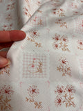 a close-up view of a fabric with a floral pattern, featuring various shades of pink and brown flowers and leaves. The fabric appears to be made of a soft, white material, and the pattern is intricate and detailed.