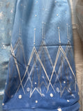 a blue fabric with a white pattern, featuring a repeating design of snowflakes and lines. The fabric appears to be a piece of clothing or textile with a winter-themed design.